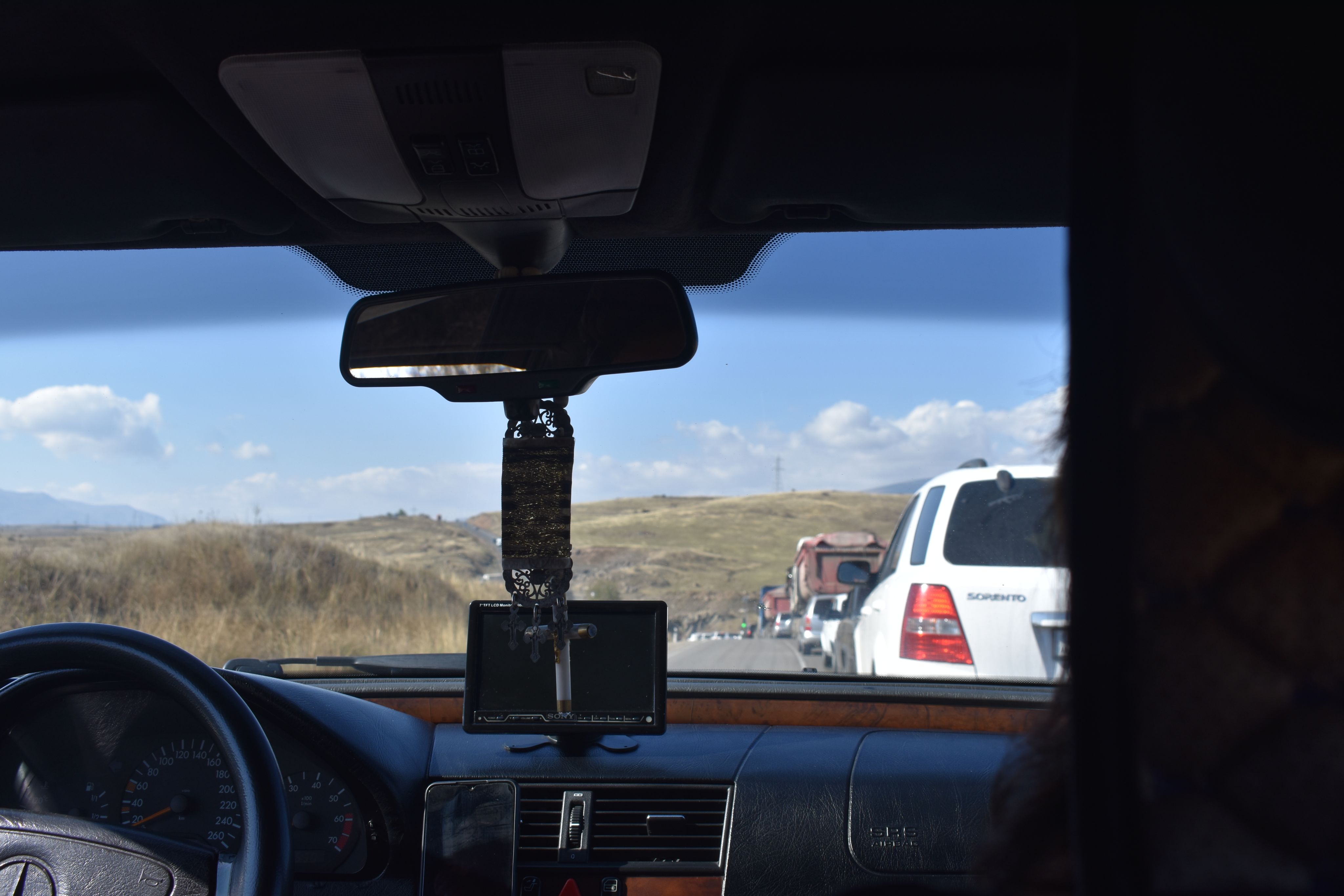 Crucifix hanging from rear car mirror with a line of cars stretching ahead.